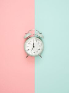 A vintage round clock on a split pastel pink and blue background.