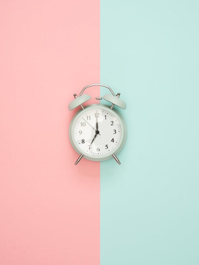 A vintage round clock on a split pastel pink and blue background.