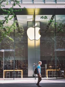 A casual scene of a man walking past the iconic glass facade of an Apple Store in Beijing, China.